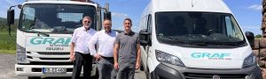 Links ein LKW in der Mitte Herr Graf senior, rechts Herr Graf junior rechts noch ein Geschäftsauto